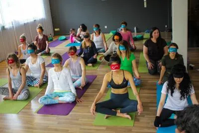 A large group of people in a yoga or meditation class sitting on mats and wearing blindfolds.