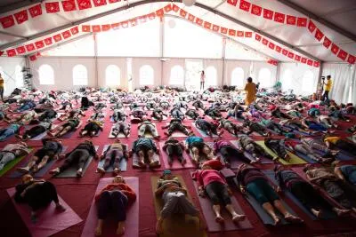 A large group of people lying on yoga mats in a tented room, with an instructor standing in the background.