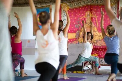 A group of people in a yoga class doing a high lunge or warrior pose with their arms raised.