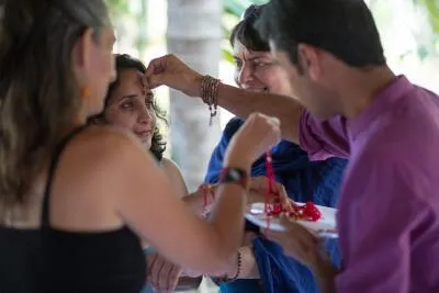 A woman applies a red bindi to the forehead of another woman in a group setting.