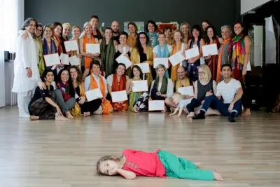 A large group of smiling adults holding certificates, with a small child lying on the floor in the foreground.