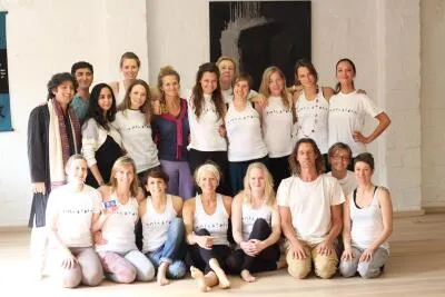 A large group of people in a bright room, posing for a group photo, likely a yoga or meditation class.