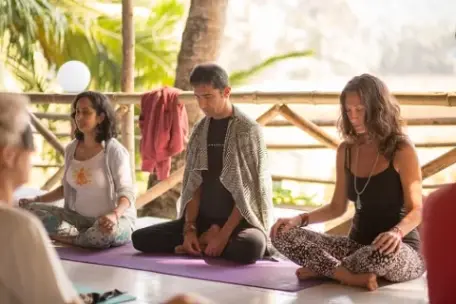 A group of people sitting in a cross-legged meditative pose on yoga mats on an outdoor deck.