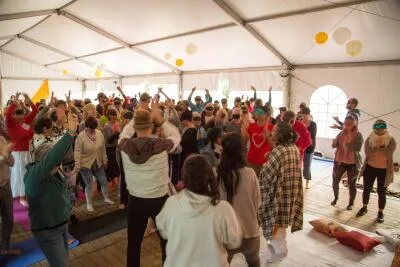 A large group of people in a tent with many wearing blindfolds and raising their hands.
