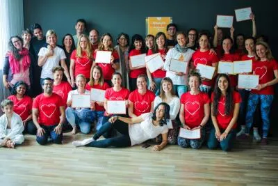 A large group of smiling adults, many wearing red shirts with a white heart, posing for a group photo and holding certificates.