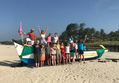 A group of people posing and smiling for a photo with a colorful boat on a sunny beach.