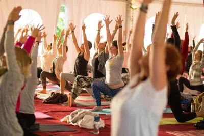 A group of people in a yoga class doing a chair pose with their arms raised.