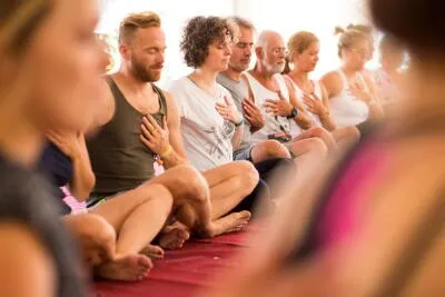 A group of people sitting in a row on the floor with their eyes closed and hands placed on their hearts.
