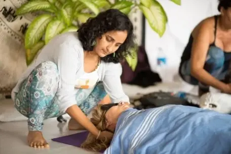 A woman performing a head massage on another person who is lying down on a mat.