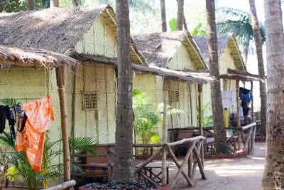 A row of thatched-roof huts with palm trees in a tropical setting.