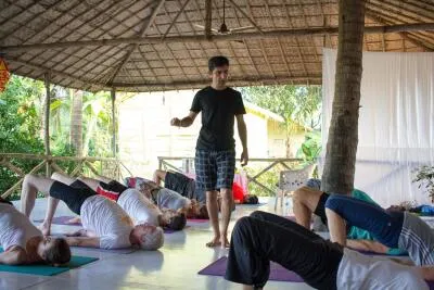A yoga instructor walks among students who are performing a bridge pose in an open-air studio.