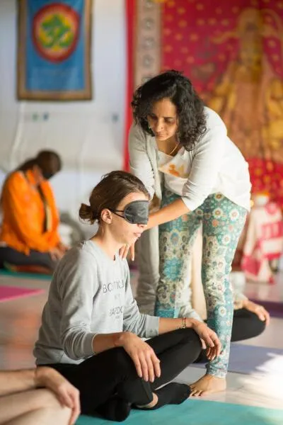 An instructor in a yoga or meditation class assisting a blindfolded student.