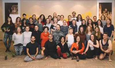 A large group of smiling adults posing for a group photo in a studio or classroom setting.