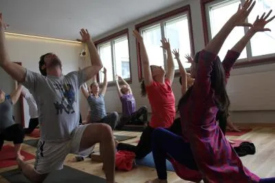 A group of people in a yoga class doing a lunge pose with their arms raised overhead.
