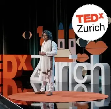 The image shows a man on a stage with a TEDx Zurich logo. The background has large letters and graphic elements.
