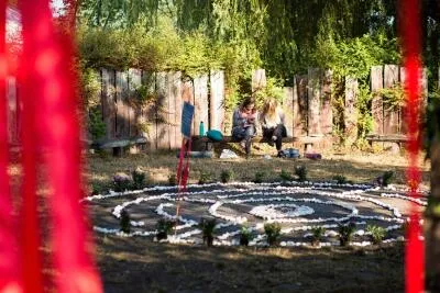 Two women sitting on a bench in a garden or outdoor setting with a circular stone and plant pattern in the foreground.