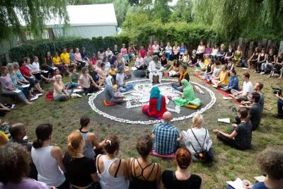 A large group of people sitting in a circle outdoors around a central teacher or leader.