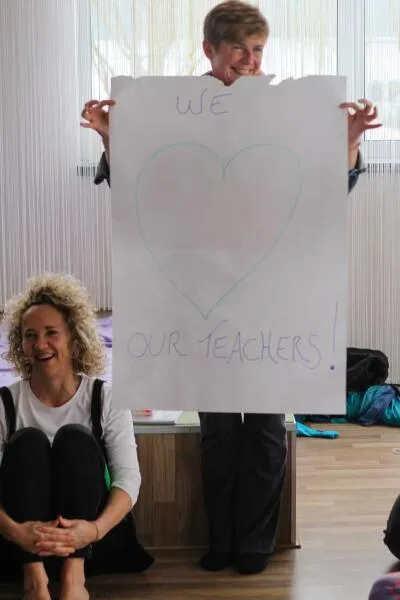A woman holding a sign that says (WE LOVE OUR TEACHERS!) while another woman smiles in front of her.