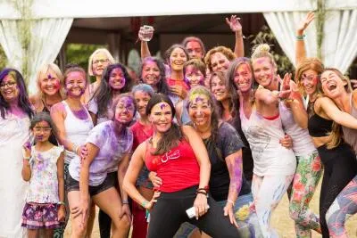 A large group of women and a child covered in colorful powder, smiling and posing for a photo.