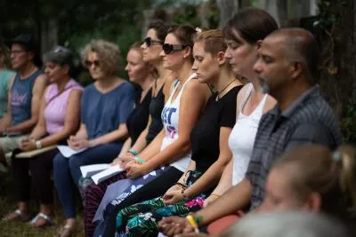 A group of people sitting in a row outdoors, with most of them having their eyes closed.