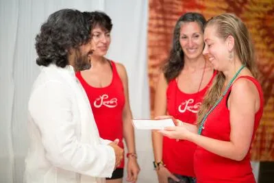 A man in a white shirt talks to three women in red shirts, one of whom is holding a booklet.