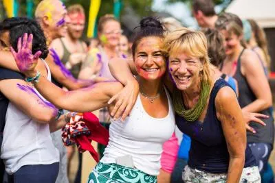 Two smiling women, covered in colorful powder, hugging during a festival.