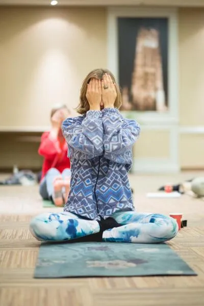 A woman sitting cross-legged on a yoga mat with her hands covering her face.
