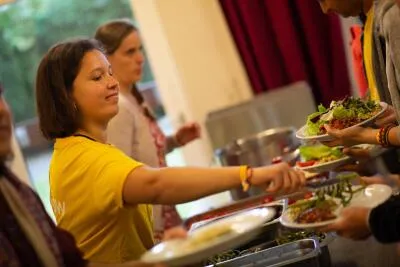 A woman in a yellow shirt serving herself food from a buffet line.