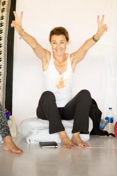 A smiling woman making peace signs with her hands while sitting on a cushion.
