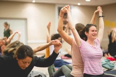 A group of people in a class, some with their arms raised, laughing and smiling.