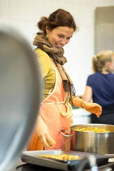 A smiling woman in a yellow shirt and apron cooking in a kitchen.