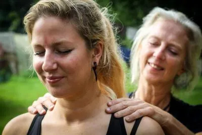 An older woman giving a younger woman a shoulder massage in an outdoor setting.