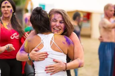Two smiling women, covered in colorful powder, hugging during a festival.