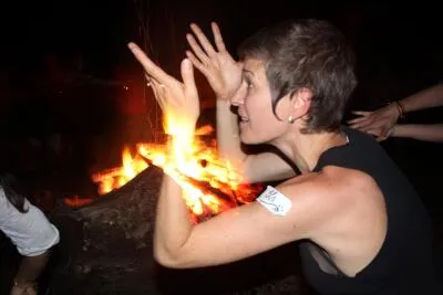 A woman with a playful expression and hands raised, illuminated by a glowing campfire at night