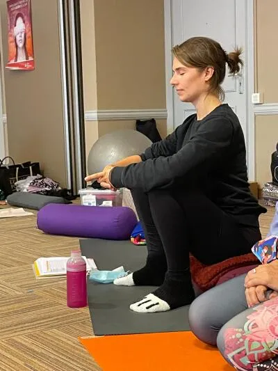 A woman with her eyes closed in a yoga pose, sitting on a mat in a crouched position.
