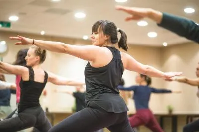 A group of people in a yoga class doing a warrior II pose.