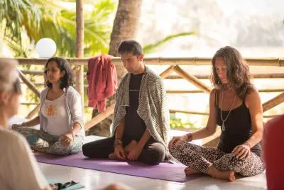 A group of people sitting cross-legged on yoga mats in an outdoor yoga class.