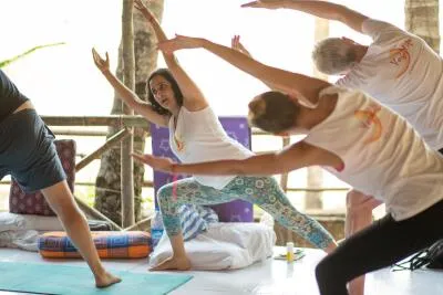 A group of people in a yoga class doing a high lunge or warrior pose with their arms raised.