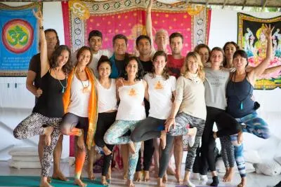 A group of smiling people in a yoga class posing together in a tree pose variation.