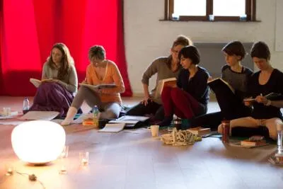 A group of women sitting on the floor in a circle, reading books and taking notes in a class or workshop.