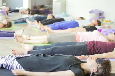 A group of people lying on their backs on yoga mats in a class, some with blindfolds on.