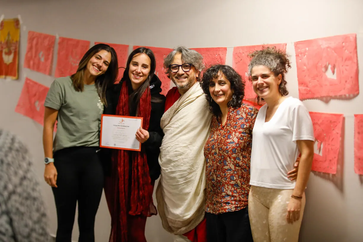 Five smiling people pose indoors with red banners in the background; one holds a certificate.