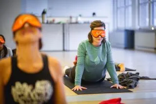 A group of people practice yoga indoors while wearing orange eye masks.