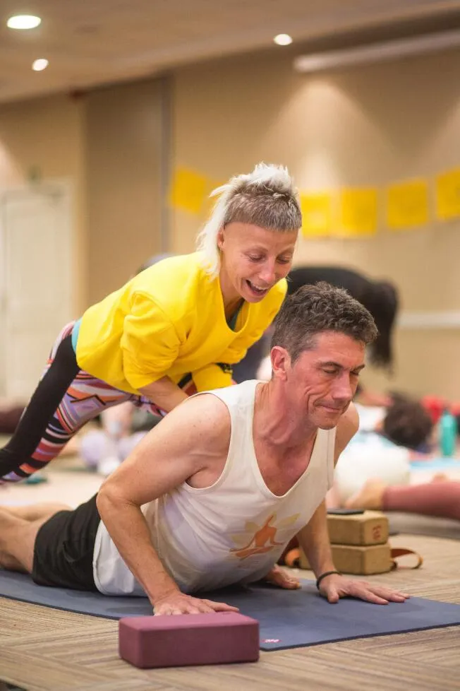 A yoga instructor assists a student in a cobra pose during a group class.
